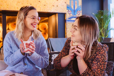 Smiling friends holding coffee talking while sitting in restaurant