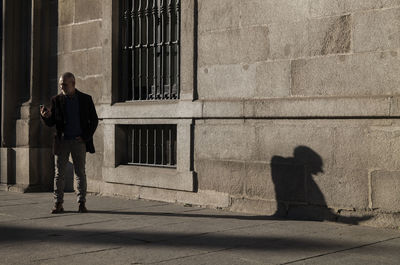 Adult man in suit looking at mobile phone against wall