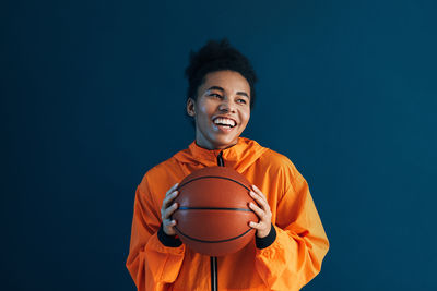 Portrait of young man playing basketball against blue background