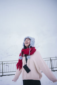 Smiling woman standing on snow covered landscape against sky during winter