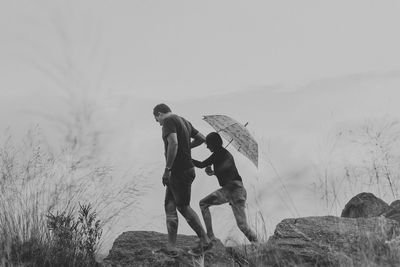 Man walking on rocks with woman holding umbrella