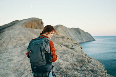 Man standing on rock by sea against sky