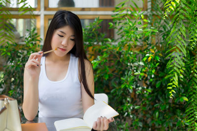Woman with pencil and book sitting at cafe against plants