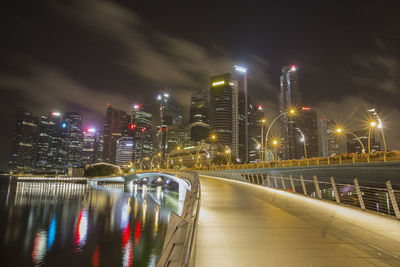 Illuminated bridge over river by buildings against sky at night