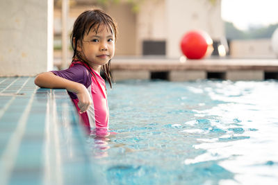 Full length of cute girl holding ball in swimming pool