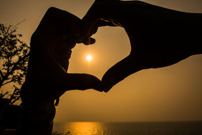 Low section of silhouette man holding hands against sky during sunset