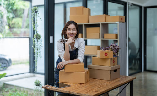 Portrait of young woman using mobile phone while sitting on window