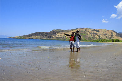 Rear view of man standing at beach against sky