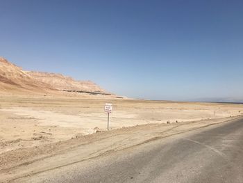 Scenic view of desert road against clear blue sky