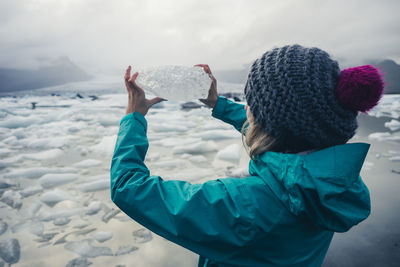 Rear view of woman standing on snow and holding a piece of ice