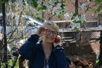 Portrait of smiling woman talking on phone while standing by tree