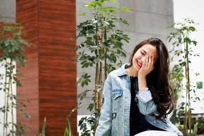 Shy woman covering face with hand while sitting against plants