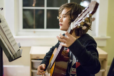 A boy studies sheet music as he practices guitar