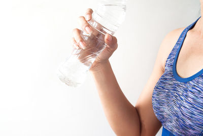 Midsection of woman holding water bottle against white background