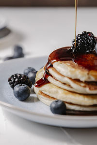 Close up of syrup pouring down a stack of pancakes with berries on top