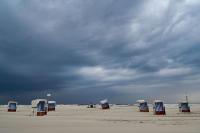 Hooded chairs on beach against sky