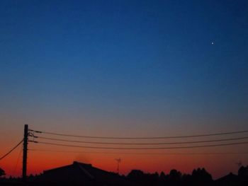 Silhouette electricity pylons against clear blue sky during sunset