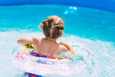 A charming little girl in a bright swimsuit learns to swim in the pool in the garden 