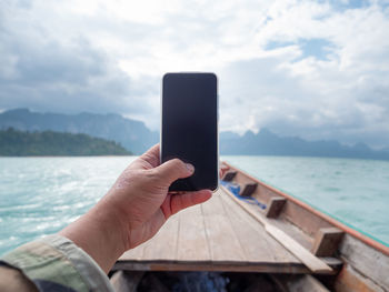 Man using mobile phone in sea against sky