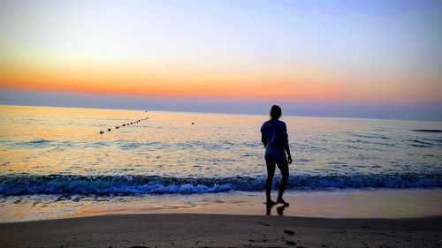 Rear view of man standing at beach during sunset