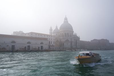 Boats in canal by buildings against sky in city