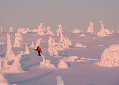 Hiker walking by ice formations on snow covered field against clear sky during winter