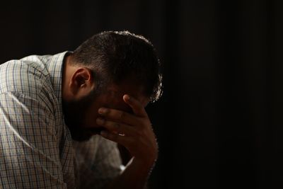 Side view of depressed man sitting against black background