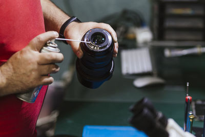 Repairman holding spray can and lens at electronics repair shop