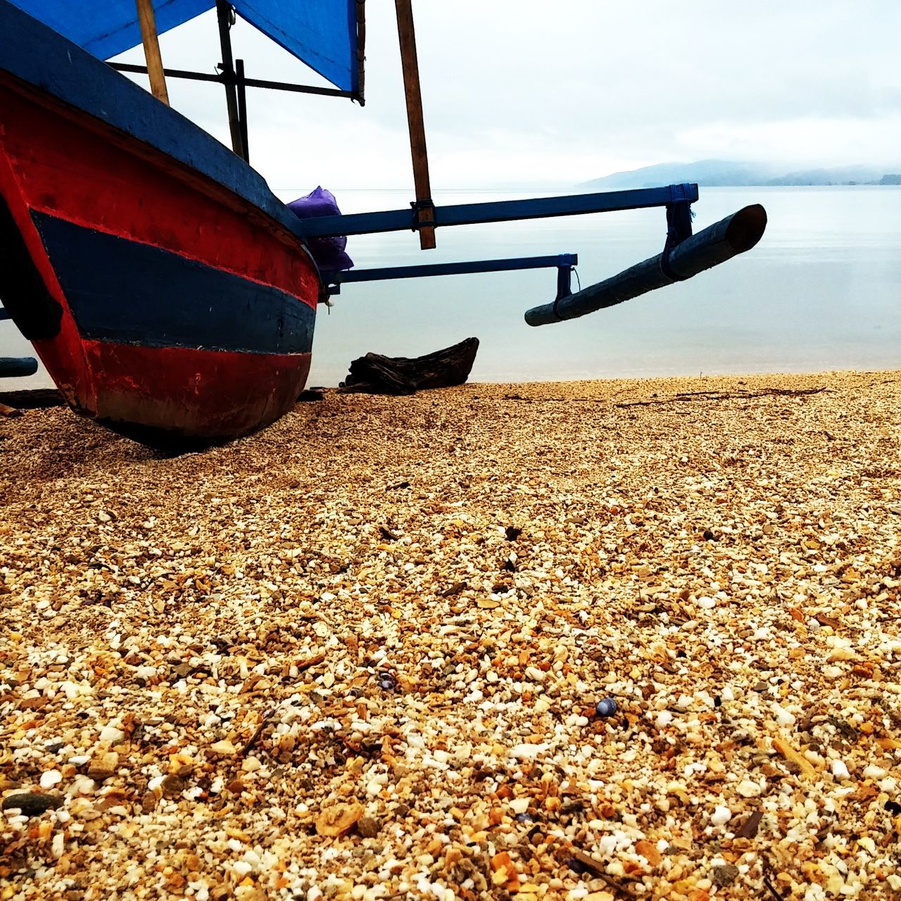 transportation, mode of transport, nautical vessel, boat, beach, part of, sand, cropped, travel, red, sea, tranquility, sky, scenics, vibrant color, tranquil scene, outdoors, shore, day, tourism, no people, nature, vacations, gravel, cloud - sky, non-urban scene