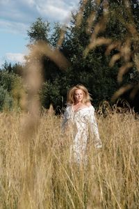 Beautiful woman standing on field against trees