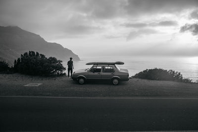 Rear view of man standing by car looking at sea