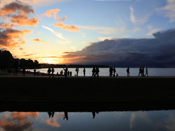 Silhouette people on beach against sky during sunset