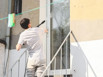 A caucasian guy in gray sports and a t-shirt from the back washes metal a ladder up