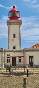 Lighthouse by building against sky