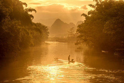 Man standing on boat in lake during sunset