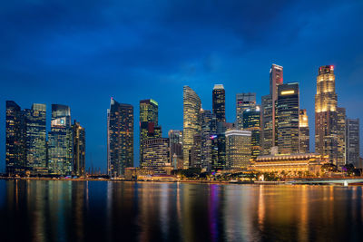 Illuminated buildings by river against sky at night