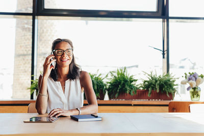 Portrait of smiling young woman using phone on table