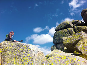 Low angle view of man sitting on rock against sky