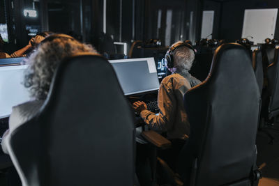 Rear view of male and female friends playing game over computers while sitting on chair