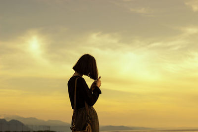 Silhouette of woman standing against sky during sunset