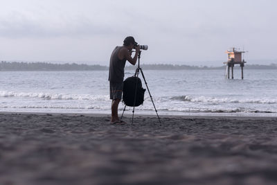 Man photographing sea while standing at beach against sky