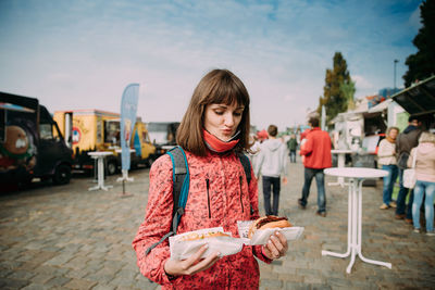 Young woman holding food on street in city against sky