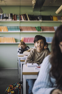 Schoolboy sitting on desk in classroom