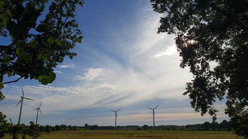 Low angle view of wind turbines on field against sky