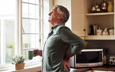 A senior man with back pain drinking a cup of tea with cbd oil