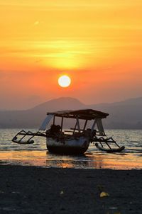 Fishing boat on beach against sky during sunset