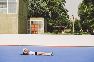 Full length of young woman with soccer ball lying on court during sunny day