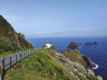 Road leading towards lighthouse by sea against clear sky