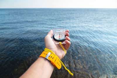 A man's hand with a wristwatch bracelet holds a magnetic compass against the background of the sea