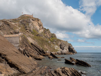 Scenic view of sea by mountain against sky in the spanish island of gaztelugatxe